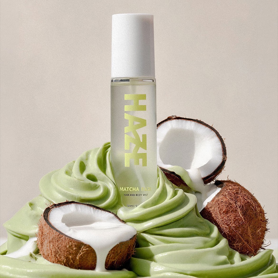 El spray para cabello y cuerpo Matcha Haze de 250 ml se presenta en un frasco transparente con tapa blanca, rodeado de cocos partidos y una crema verde.