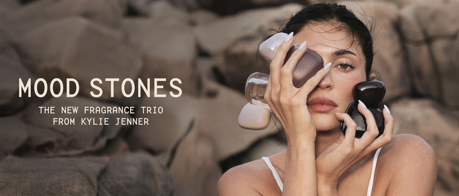 Descubre Mood Stones, el nuevo trío de fragancias de Kylie Jenner, con tres frascos de perfume de diferentes colores y formas, sostenidos por una mujer con el pelo oscuro y los labios rosados.