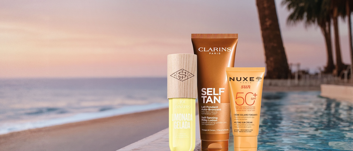 Tres productos de belleza, incluyendo una bruma perfumada Sol de Janeiro Limonada Gelada, una loción autobronceadora Clarins Self Tan y una crema solar Nuxe Sun SPF 50, se exhiben junto a una piscina con palmeras y el mar al atardecer.