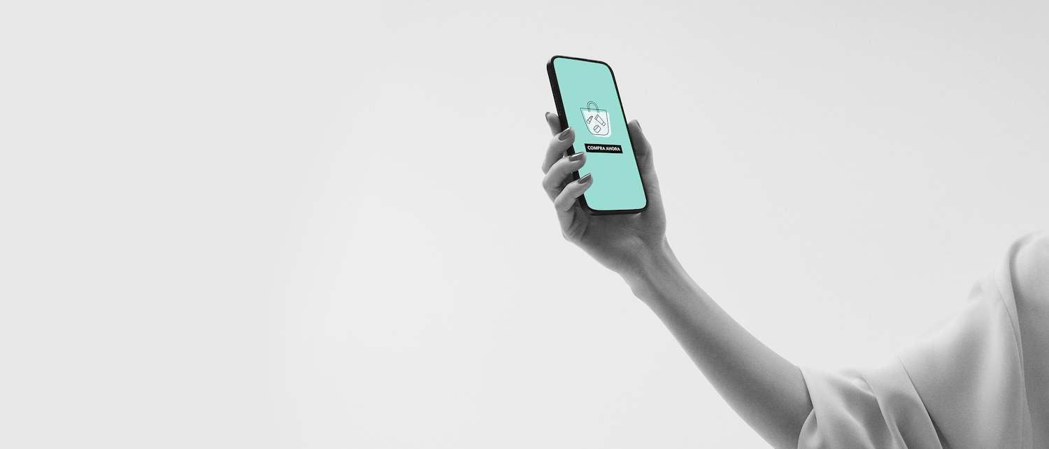 Una mano sostiene un teléfono móvil con una bolsa de compras y el texto "Compra Ahora" en la pantalla, invitándote a explorar las últimas ofertas.